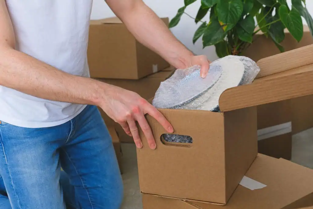 Person wrapping plates in bubble wrap and packing them into a cardboard box
